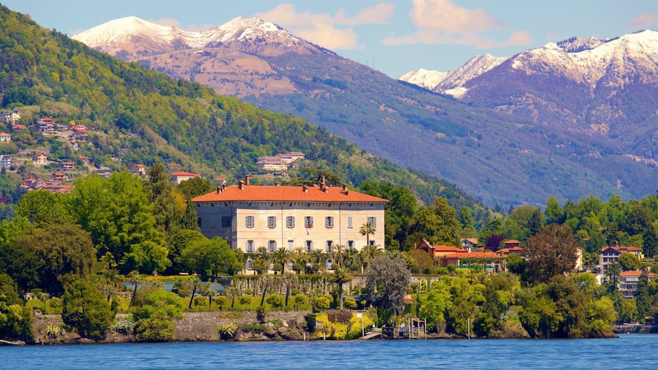 A lakeside town with a prominent building, lush greenery, and snow-capped mountains in the background.