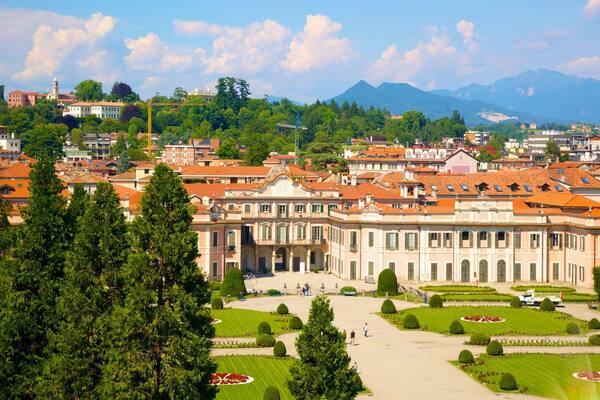 A historic building with a large courtyard surrounded by trees and manicured gardens.