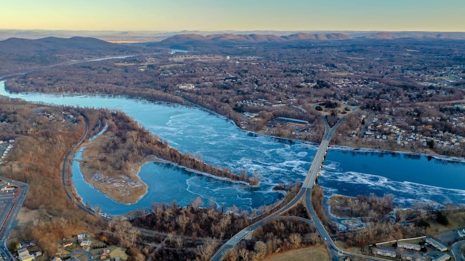 An aerial view of a river winding through a town with surrounding hills.