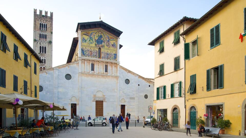 Una plaza histórica con una iglesia destacada que presenta un mosaico colorido, rodeada de edificios tradicionales con contraventanas verdes.