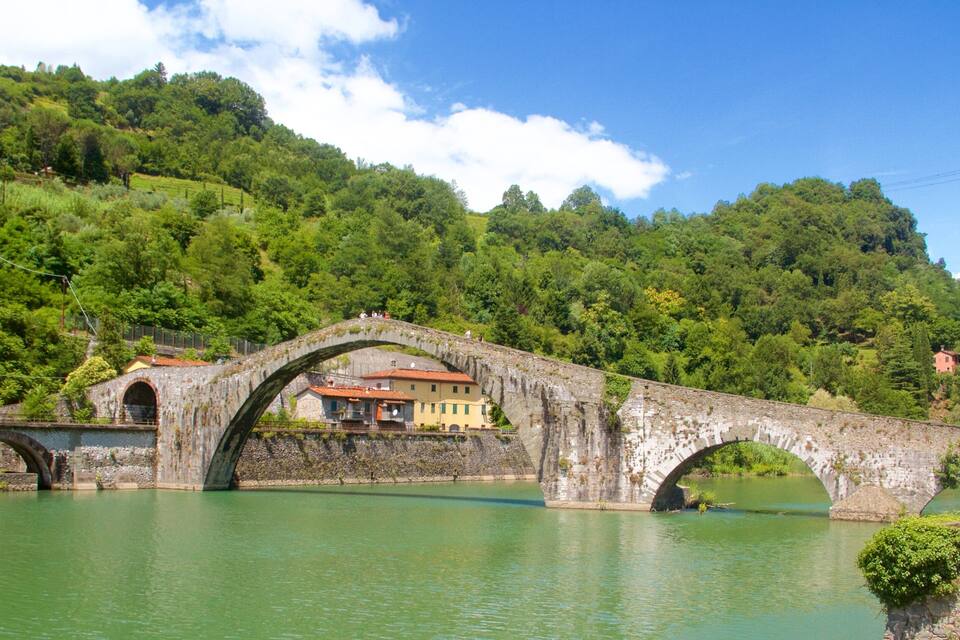 A stone bridge over a river with houses on the hillside.