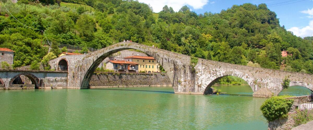 A stone bridge over a river with houses on the hillside.