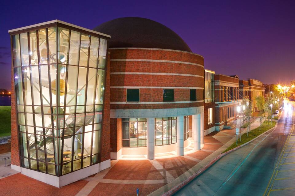 A modern building with a glass atrium and a dome structure at night.