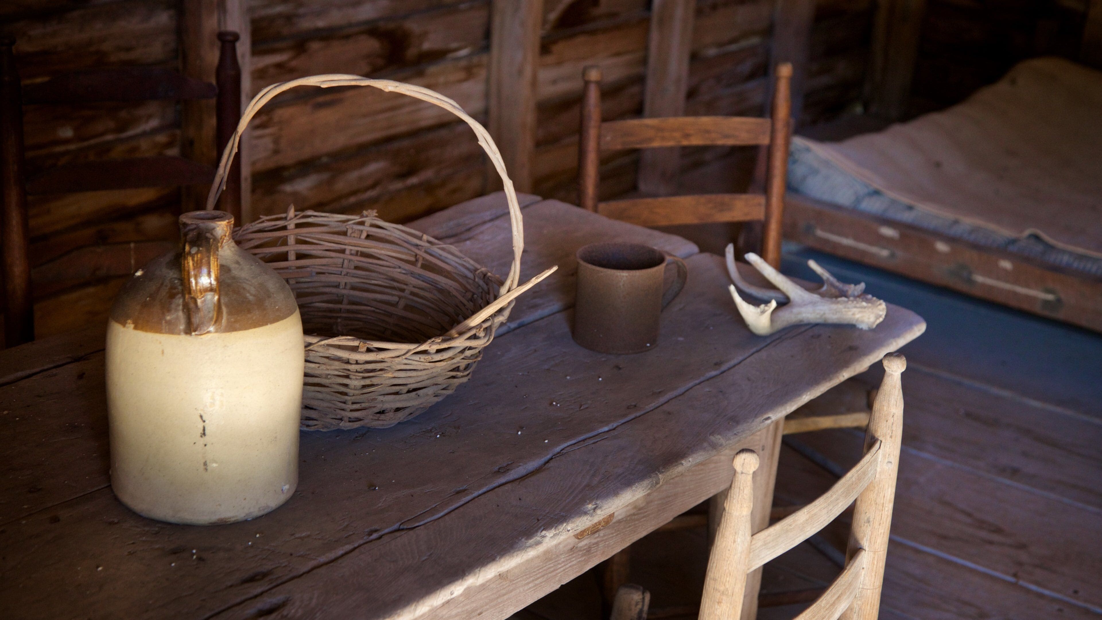 Una mesa de madera rústica con una cesta tejida, una taza de cerámica y una botella de vidrio.