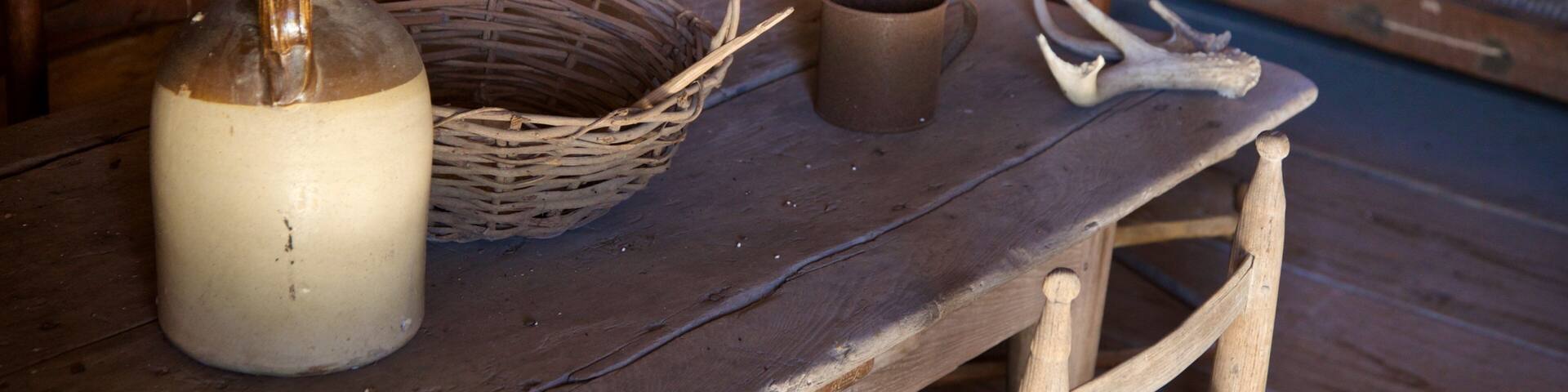 A rustic wooden table with a woven basket, a ceramic mug, and a glass bottle.