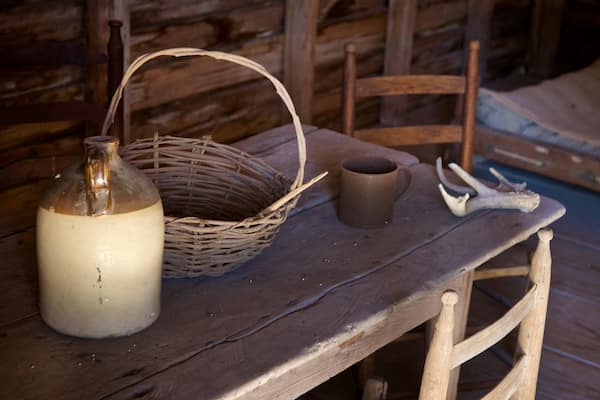 A rustic wooden table with a woven basket, a ceramic mug, and a glass bottle.