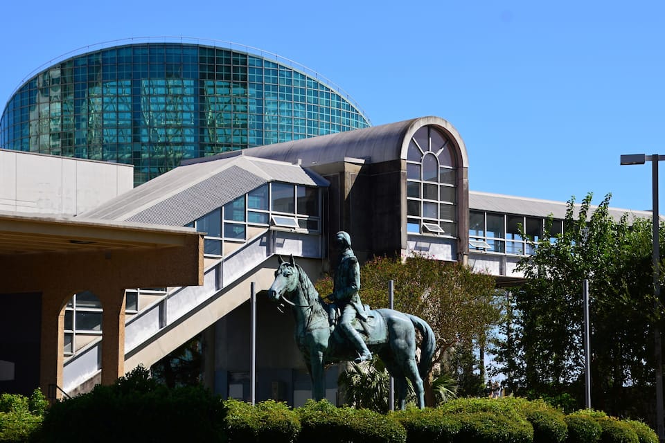 Um edifício moderno com cúpula de vidro e uma estátua de um homem montado a cavalo em frente.