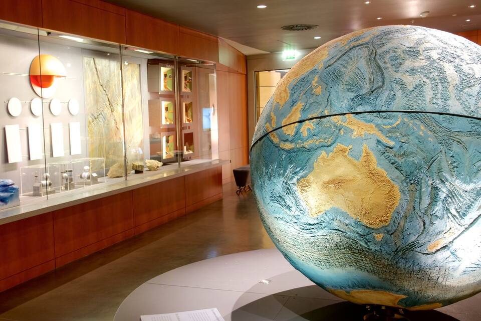 Une exposition de musée comprenant un grand globe terrestre mettant en valeur l’Australie, un mur présentant divers échantillons géologiques et une collection d’objets d’art de forme circulaire.