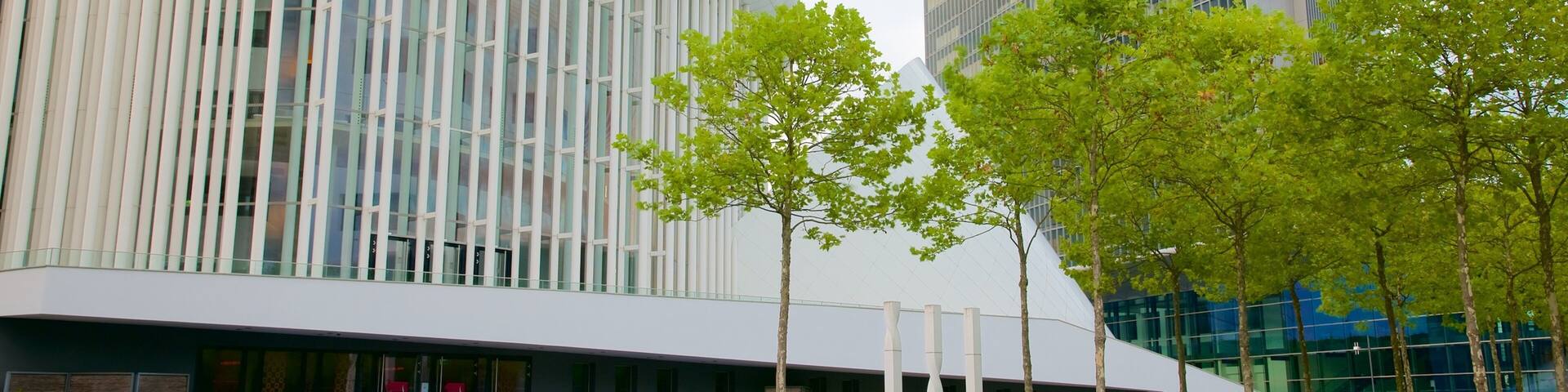 A modern building with a curved facade and vertical lines, surrounded by trees and another tall building in the background.