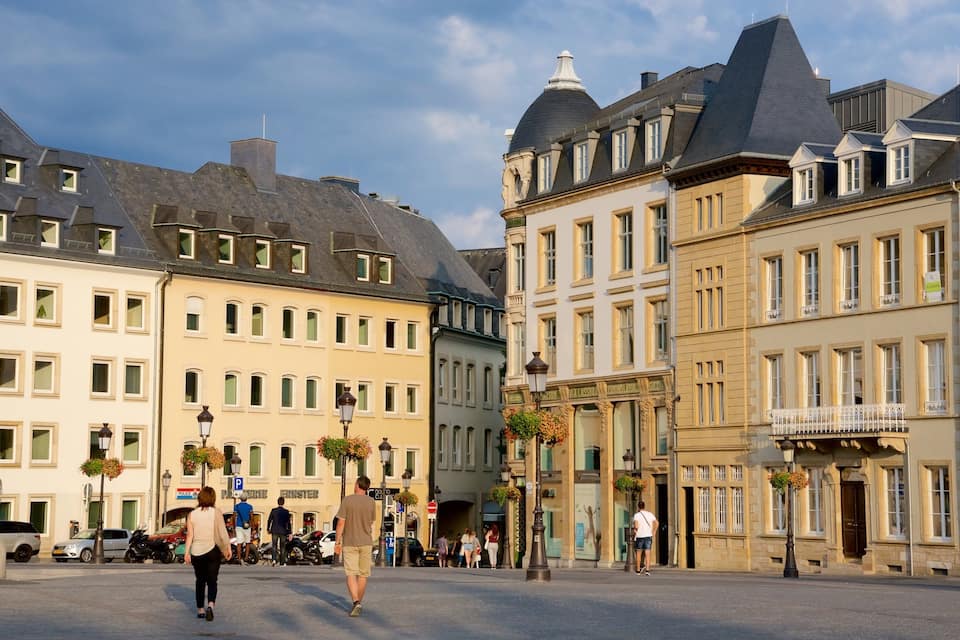 Een Europees stadsplein met historische gebouwen, voetgangers en geparkeerde auto's.