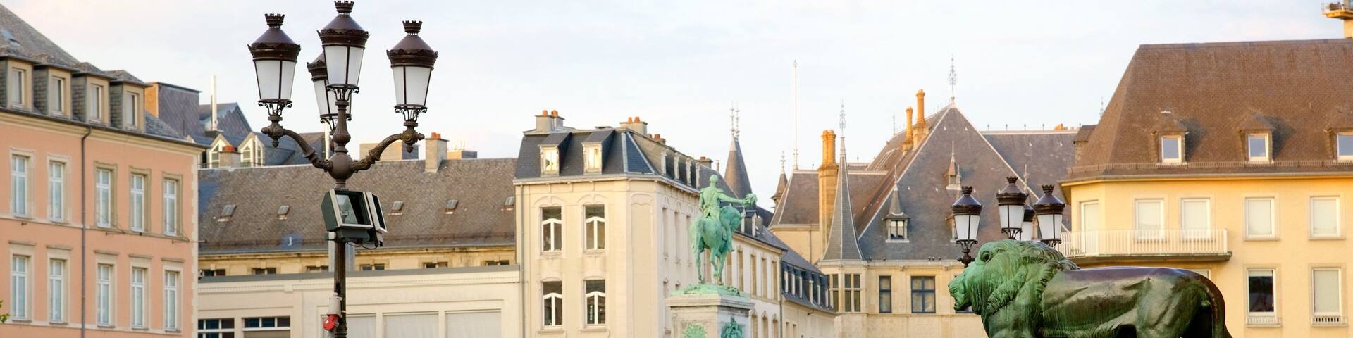 A historic square with a lion statue, old buildings, and a yellow barricade.