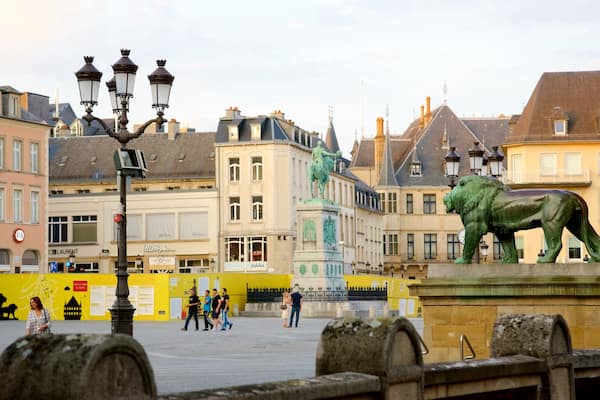 A historic square with a lion statue, old buildings, and a yellow barricade.