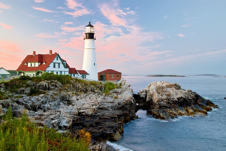 A lighthouse and houses on a rocky coastline with the ocean in the background.