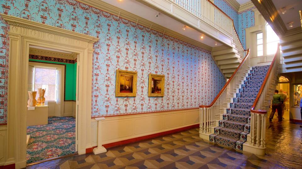 A grand hallway with ornate wallpaper, a patterned carpet, and a staircase with a red handrail.