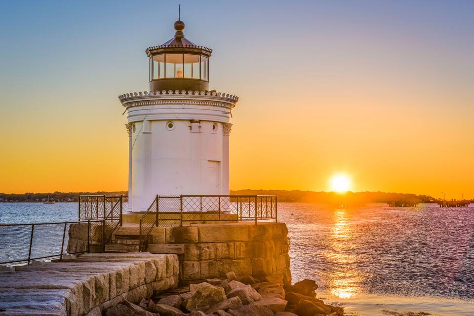 Un phare au coucher du soleil, au bord de l’eau.