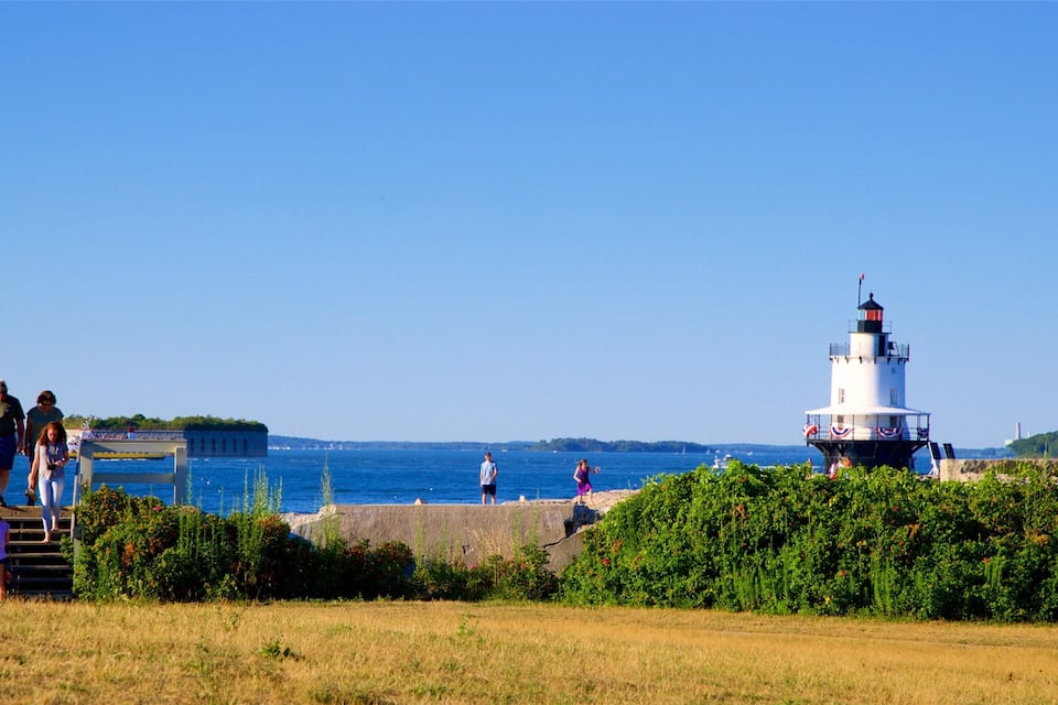 Un phare, une jetée et des personnes se promenant le long de la plage.
