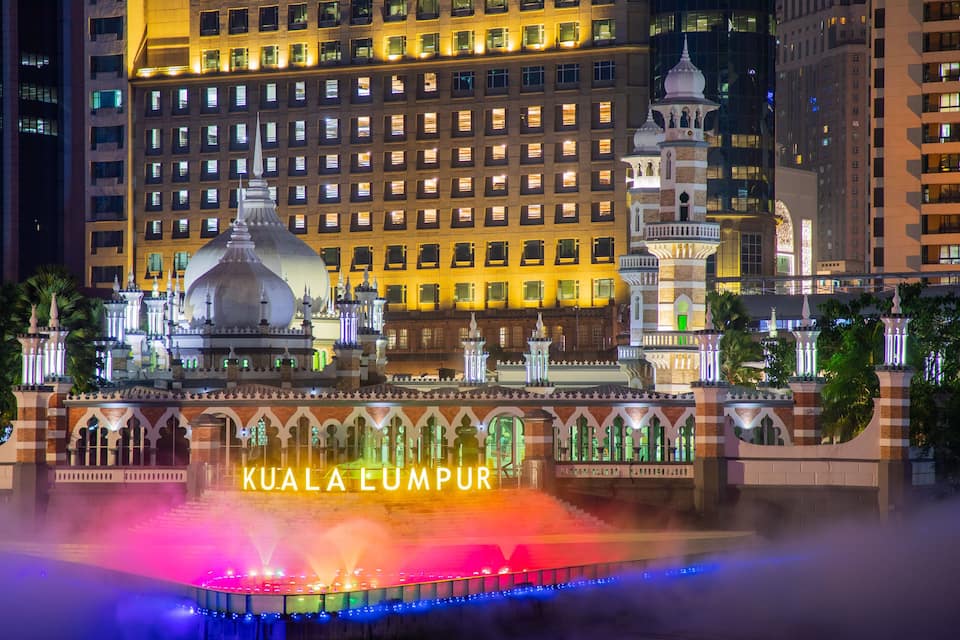 Una vista nocturna de les Torres Petronas de Kuala Lumpur amb una font colorida al primer pla.