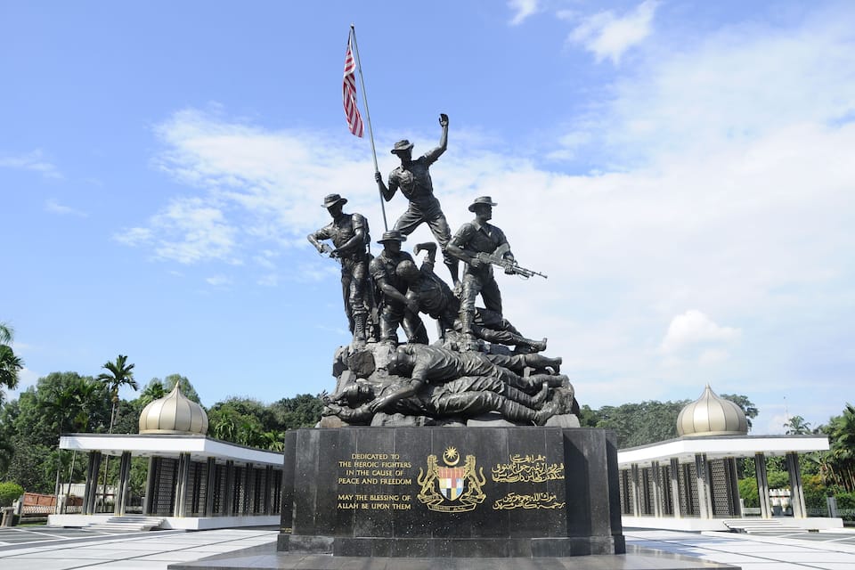 Monument de guerra amb una estàtua de soldats, una bandera i una placa commemorativa.