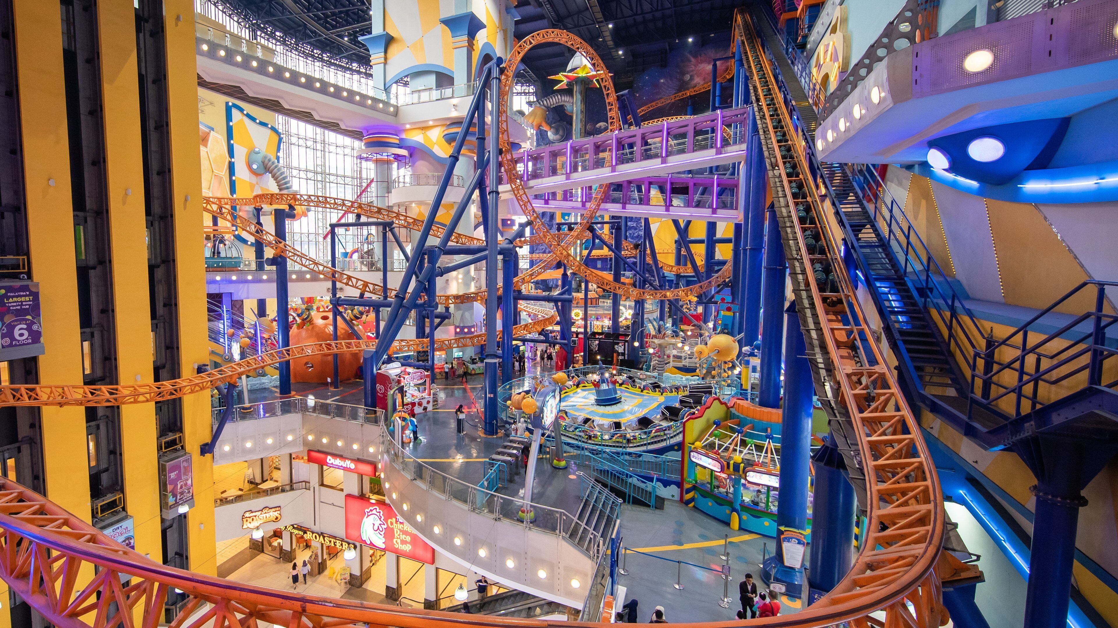 Parque de atracciones cubierto con montañas rusas, noria y diversas tiendas.