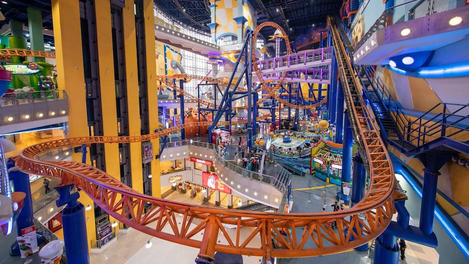 An indoor amusement park with a roller coaster, escalators, and various shops.