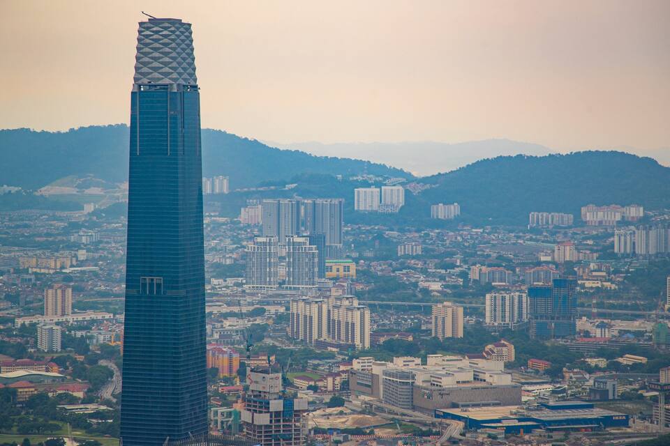 A cityscape with a prominent skyscraper, numerous residential and commercial buildings, and a hilly backdrop.