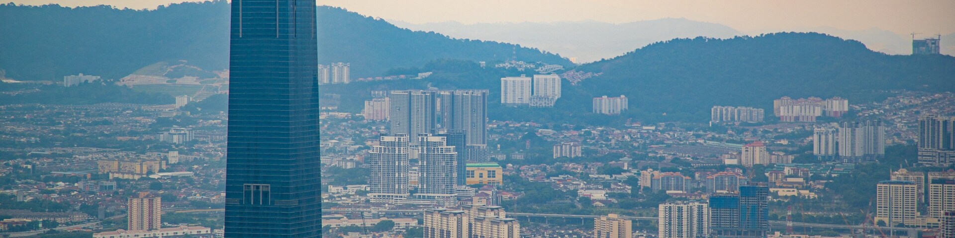 Paisagem urbana com um arranha-céu imponente, vários edifícios residenciais e comerciais, e um relevo montanhoso ao fundo.