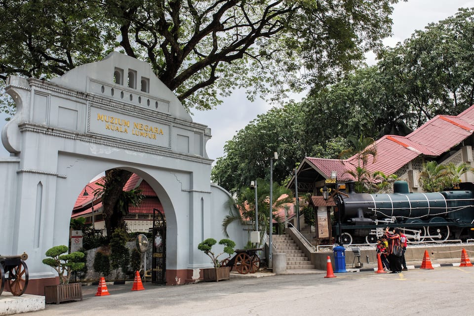 A white archway with the text "MUZIUM NEGA RAYA KUALA LUMPUR" and a black steam locomotive in the background.