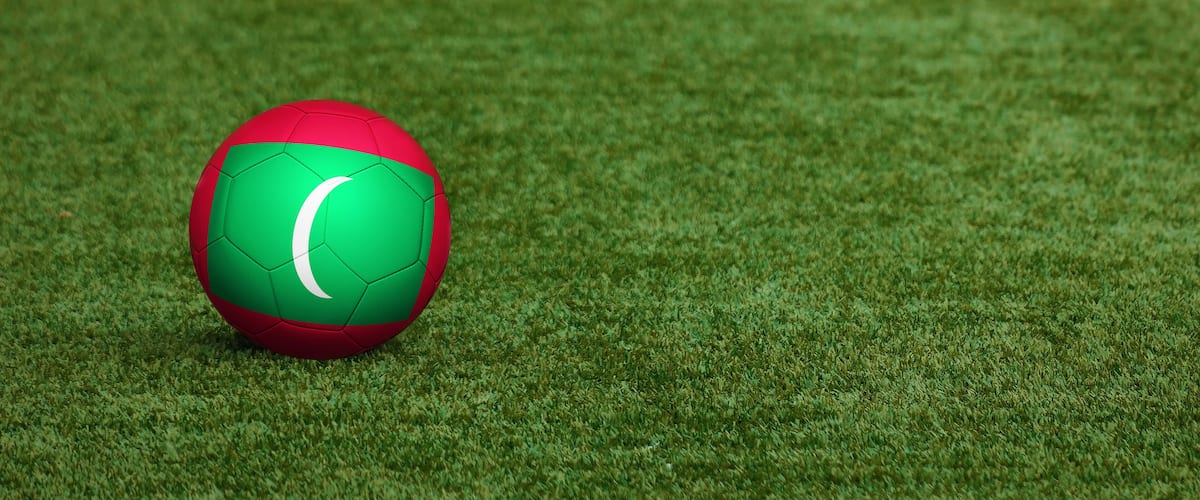 Maldives flag on ball at soccer field background. National football theme on green grass. Sports competition concept.