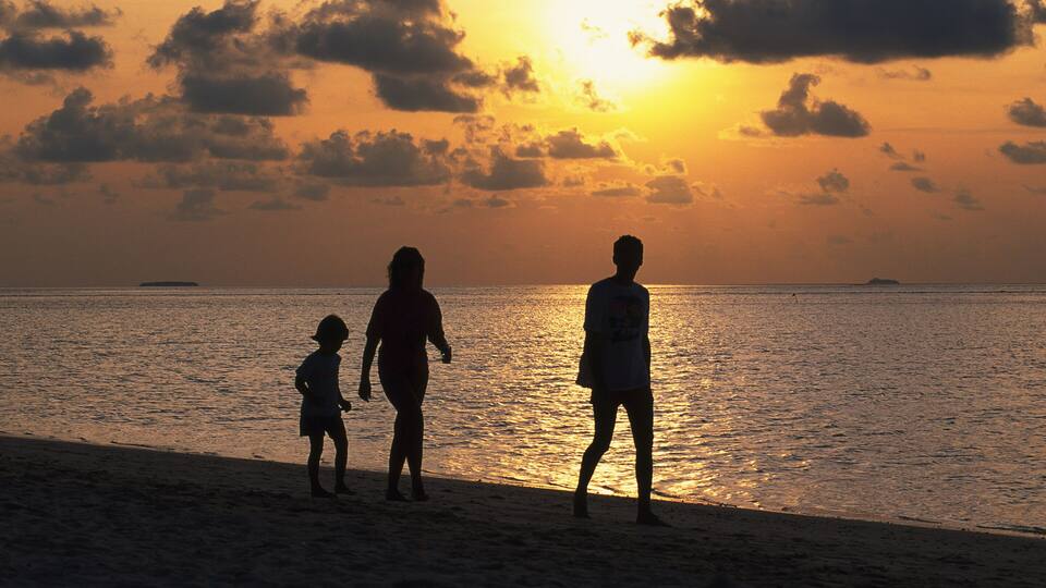 A sunset over the ocean with silhouettes of people on the beach.