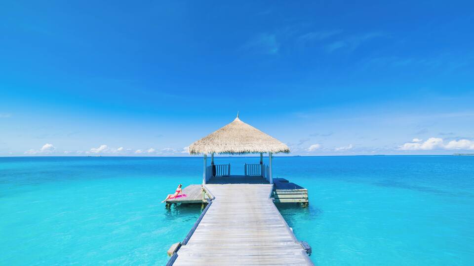 A wooden pier leading to a thatched-roof structure over turquoise ocean waters.