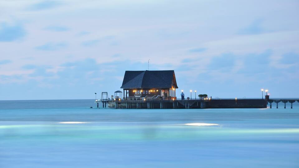 A pier with a small building and lights at dusk.