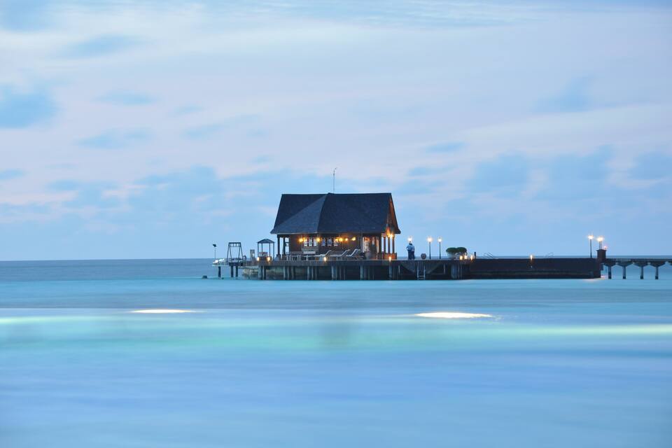 A pier with a small building and lights at dusk.