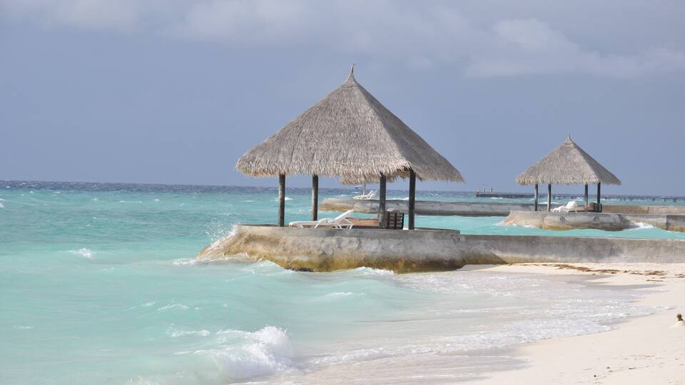 A beach with thatched umbrellas and lounge chairs.