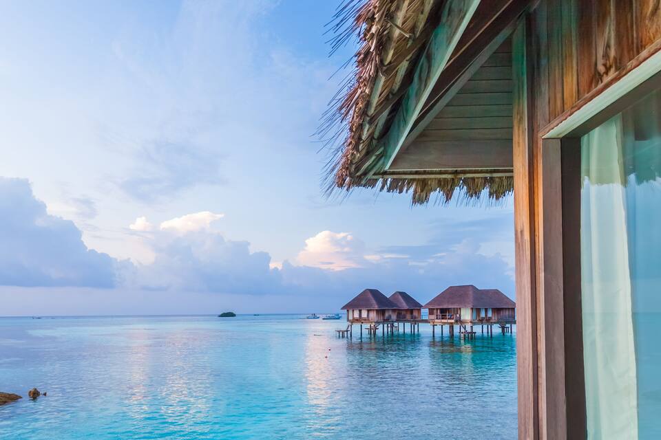Overwater bungalows, clear turquoise water, and a partly cloudy sky.