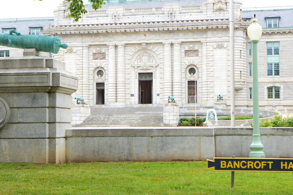 A large building with ornate architecture, a cannon, and a sign reading "Bancroft Hall".
