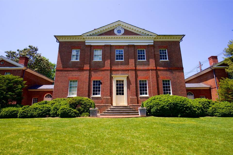 A large red brick building with a central entrance, flanked by two smaller buildings, surrounded by well-maintained lawns and trees.