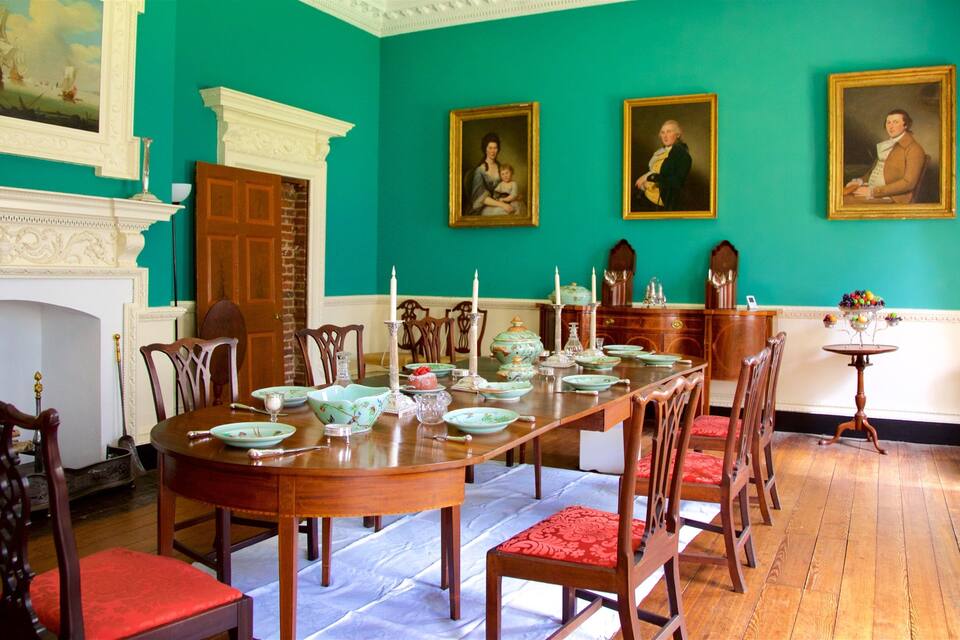 Una sala de dinar formal amb una taula de fusta llarga preparada per a un àpat, envoltada de cadires amb coixins vermells.