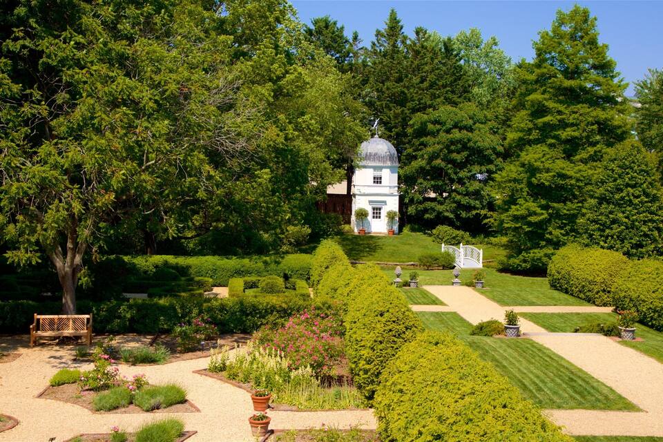 Un edifici blanc amb una cúpula, envoltat de vegetació exuberant i un jardí ben cuidat amb camins i bancs.