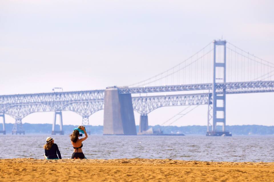 A beach with two people, a large suspension bridge in the background.
