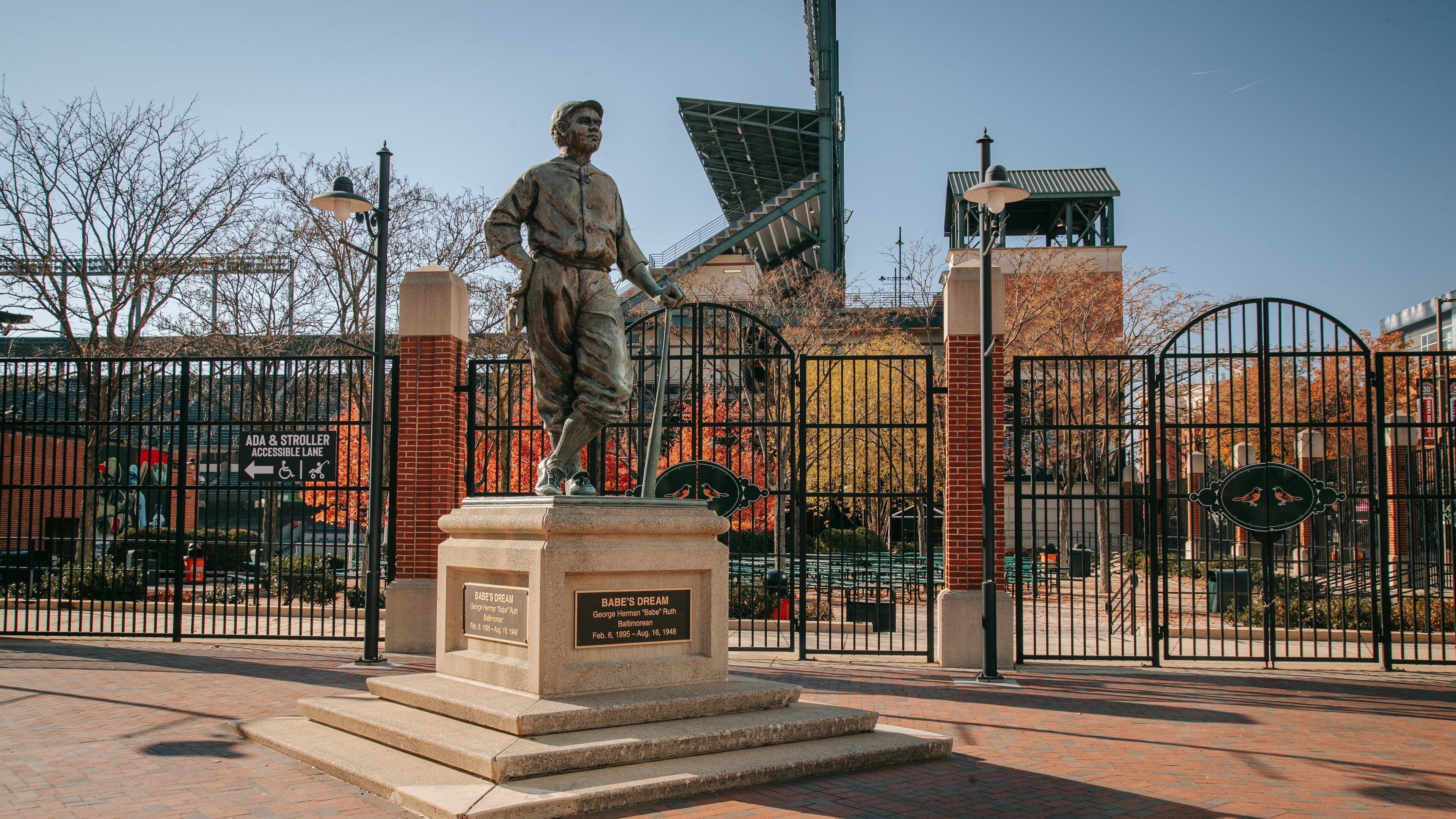 Una estàtua de Babe Ruth a un parc, amb un mur de maó i unes reixes metàl·liques al fons.
