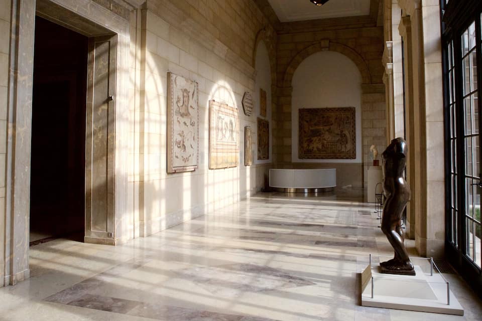 A marble hallway with a sculpture, a large painting, and a white pedestal.