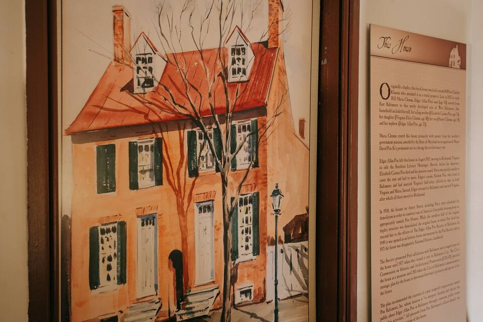 A watercolor painting of a historic house with a red roof and green shutters, alongside a detailed informational plaque.