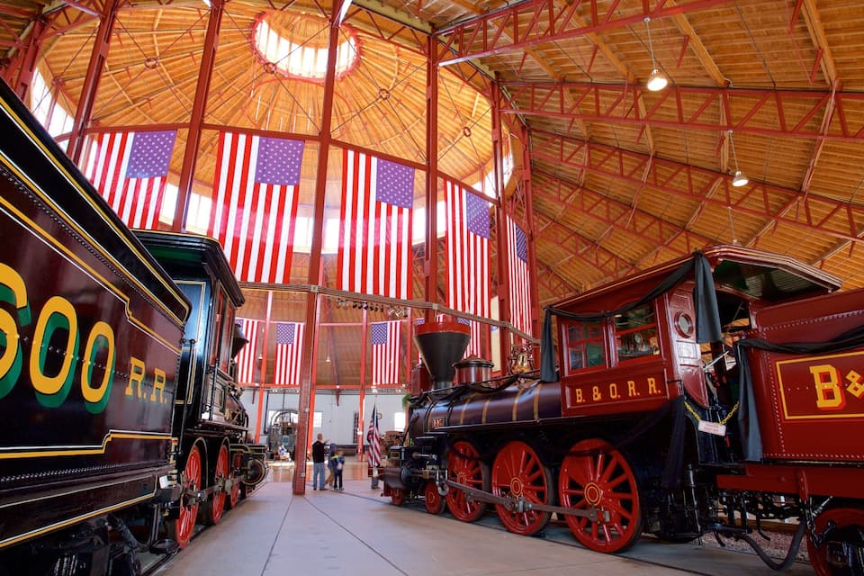 Vintage steam locomotives inside a large, open-roofed building with American flags.