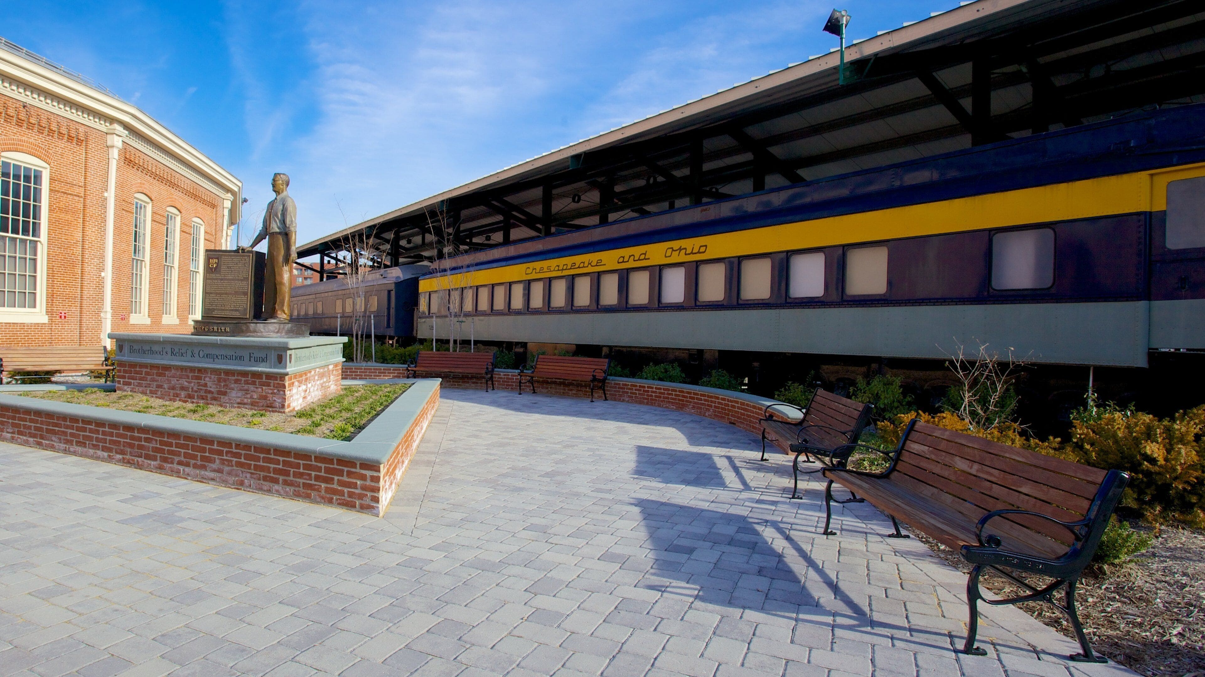 Una estación de tren con una estatua, bancos y un edificio de ladrillo.