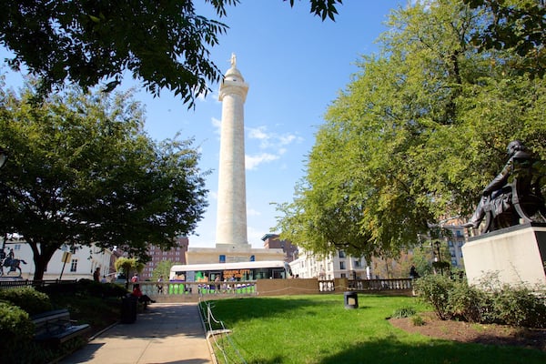 Ein hohes, weißes Denkmal, umgeben von Bäumen und Bänken in einem Park.