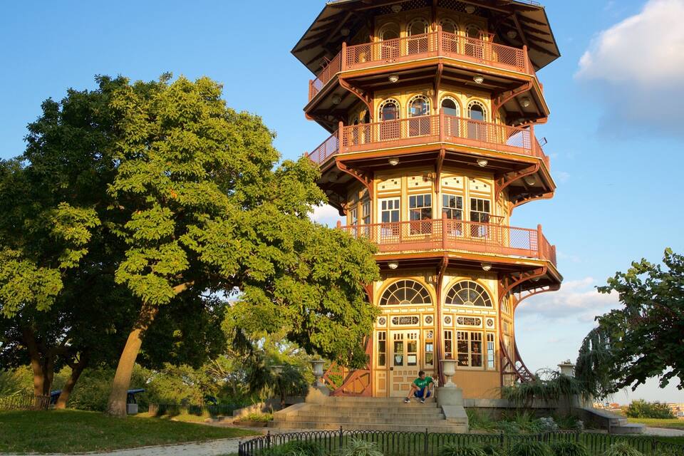 A multi-tiered tower with ornate balconies and large windows, surrounded by lush green trees.