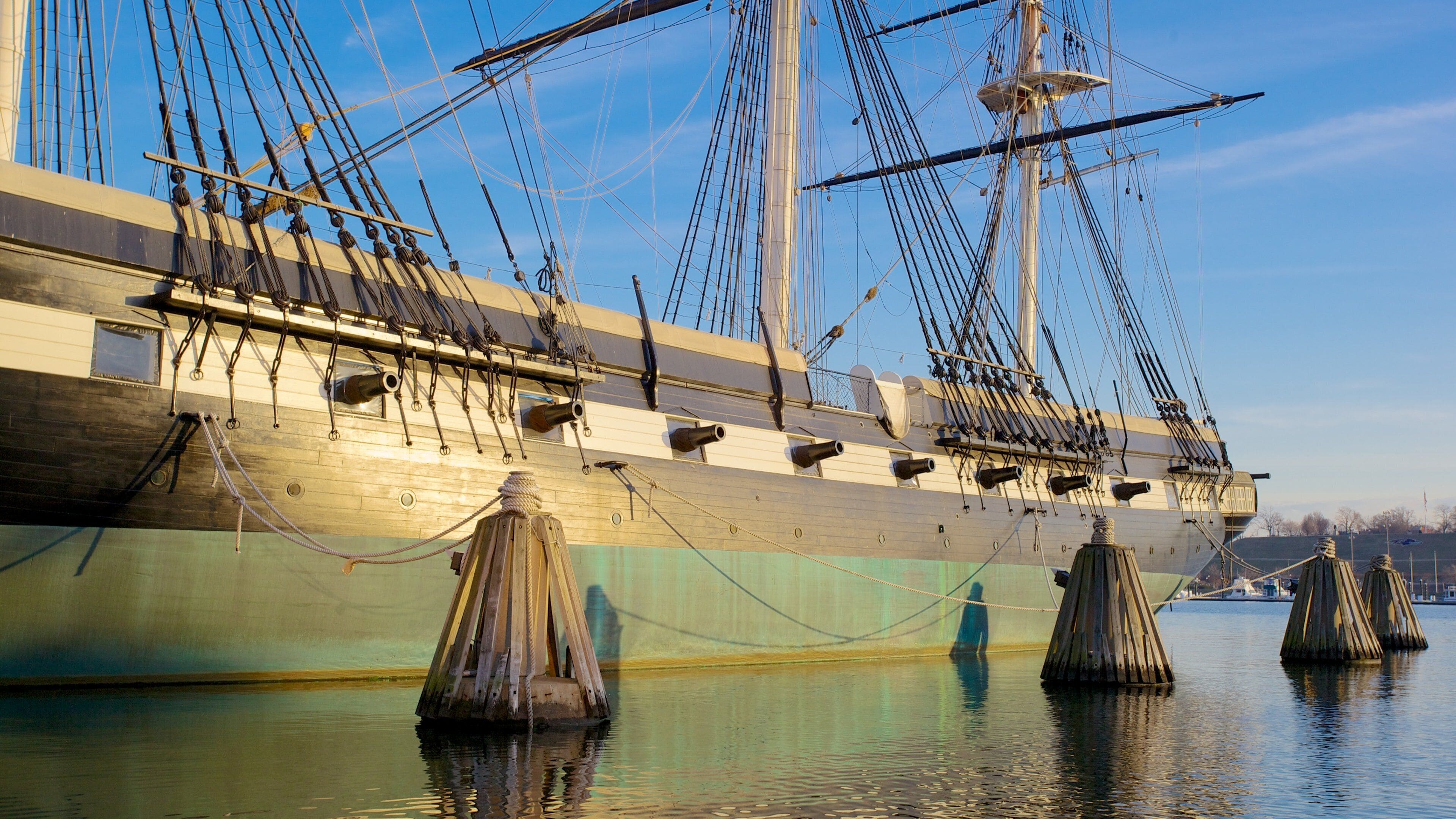 Historic USS Constellation docked in Baltimore, Maryland on a clear sunny day with calm waters and visible masts