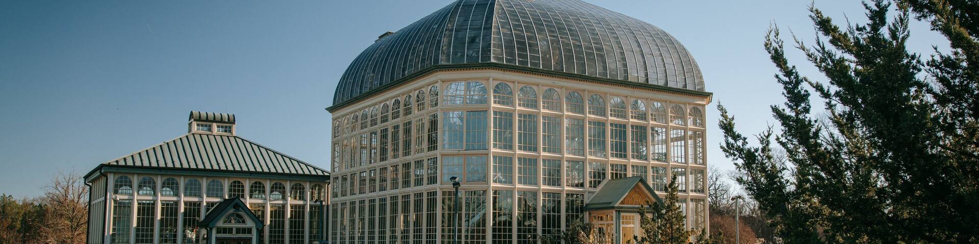 A large glass-domed greenhouse with a smaller attached structure, surrounded by a grassy area and trees.