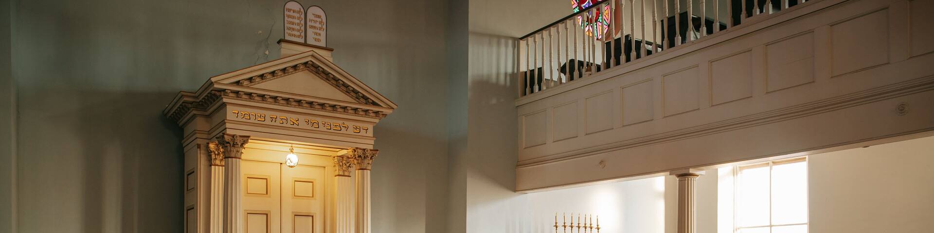 A synagogue interior with wooden benches, a Torah ark, and a candelabrum.