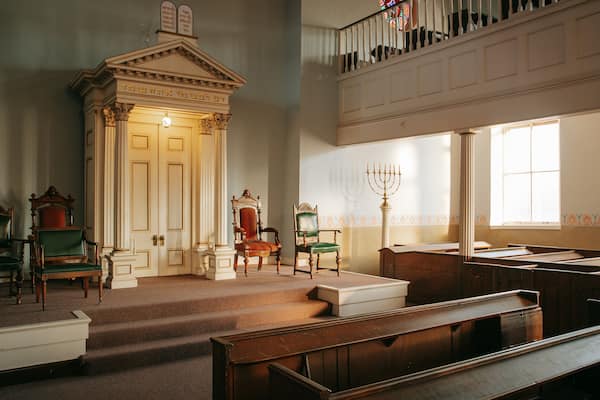 A synagogue interior with wooden benches, a Torah ark, and a candelabrum.